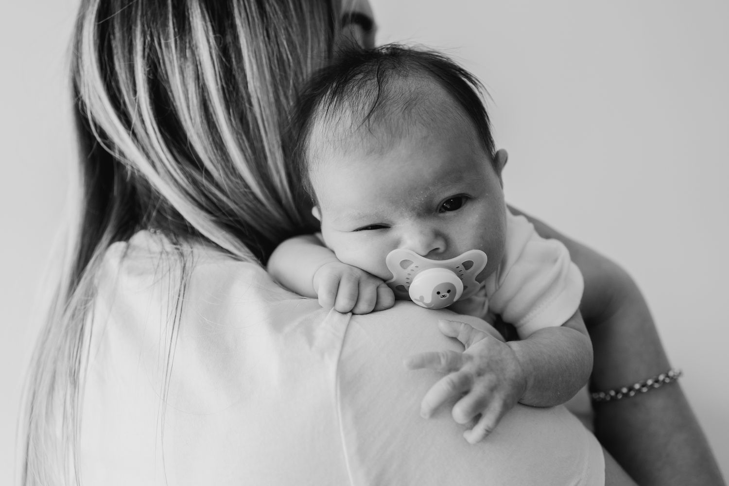 Baby with pacifier resting on adult's shoulder in black and white.
