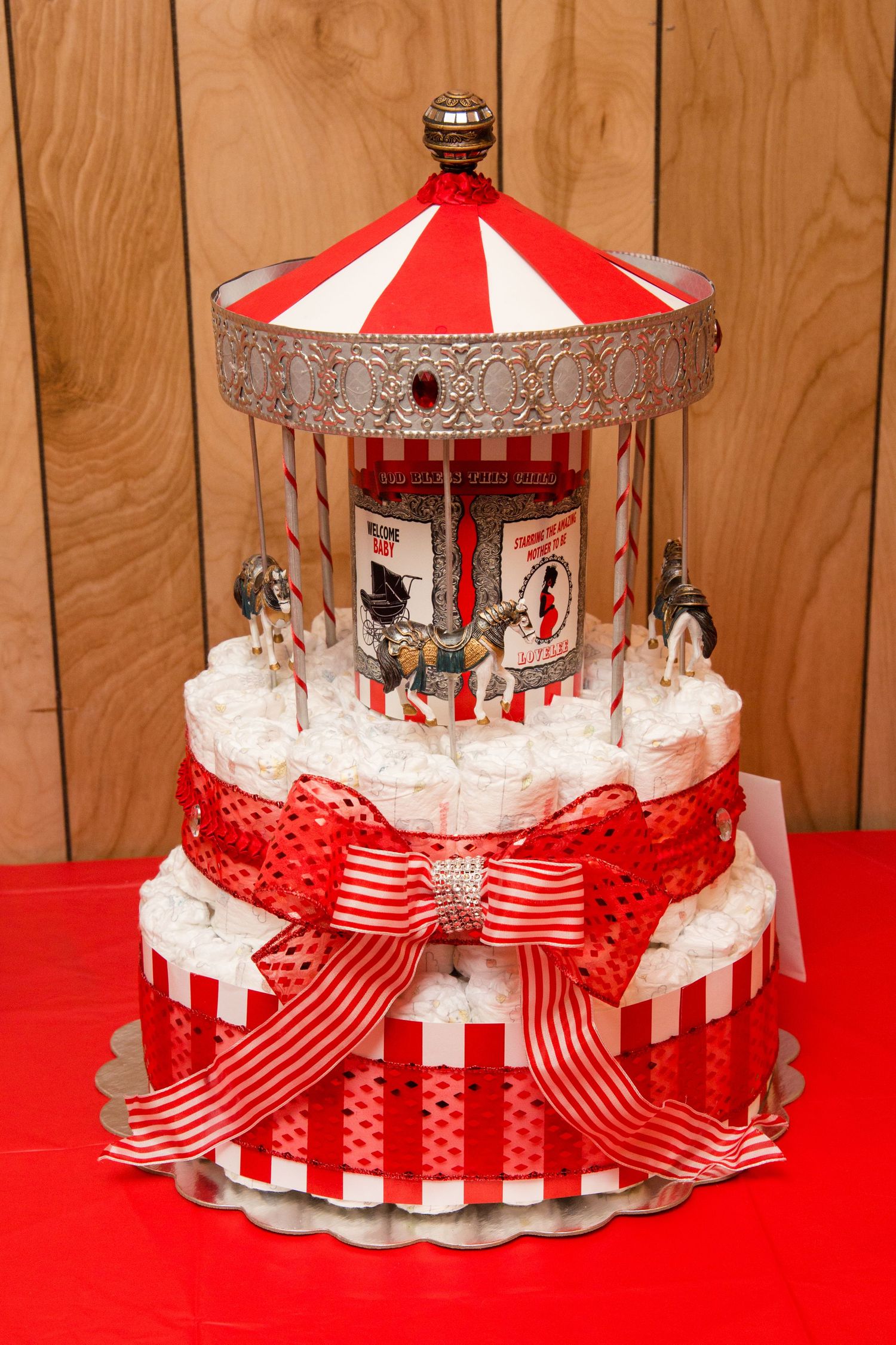 A red and white striped carousel-themed cake or diaper display with decorative ribbon and lace trim.
