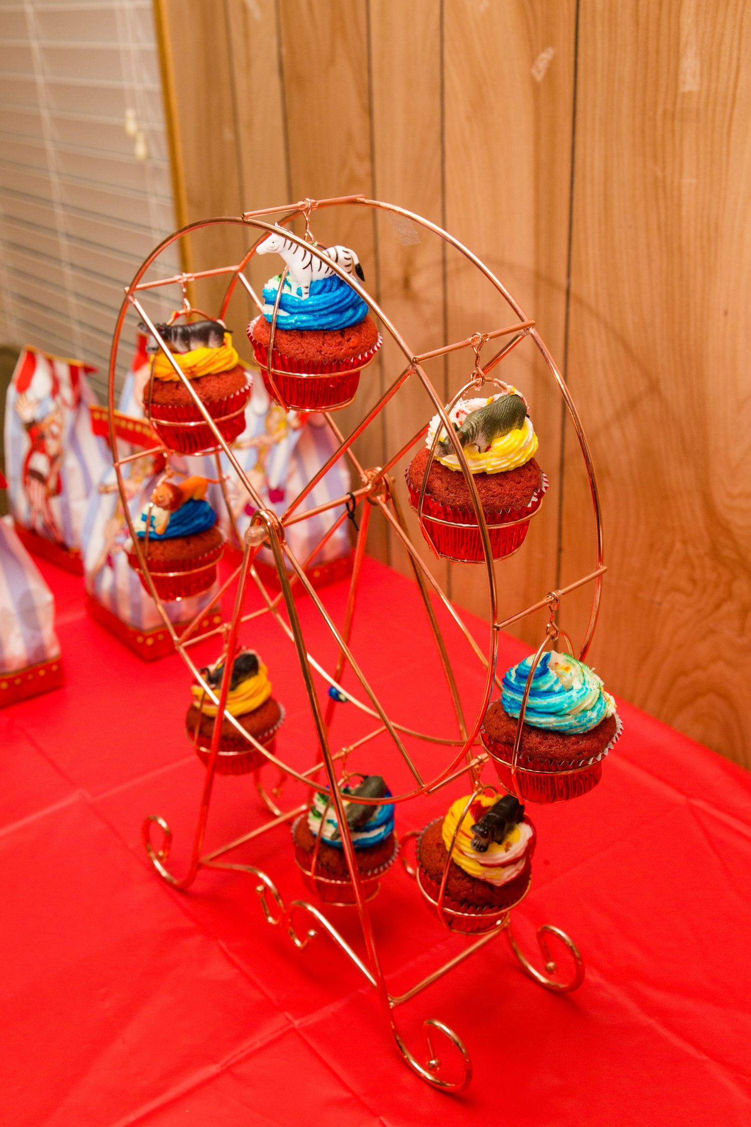 Colorful miniature Ferris wheel display with cupcakes on a red tablecloth.