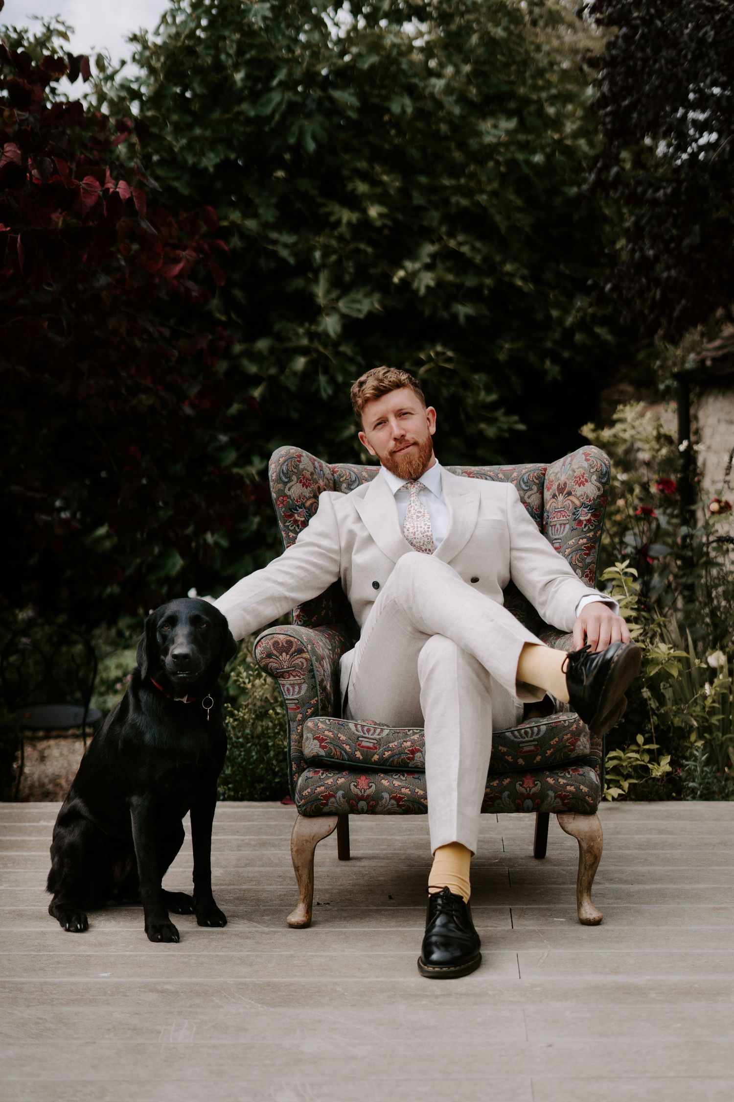 groom sat in armchair in gardens with his dog before the wedding ceremony in oxfordshire