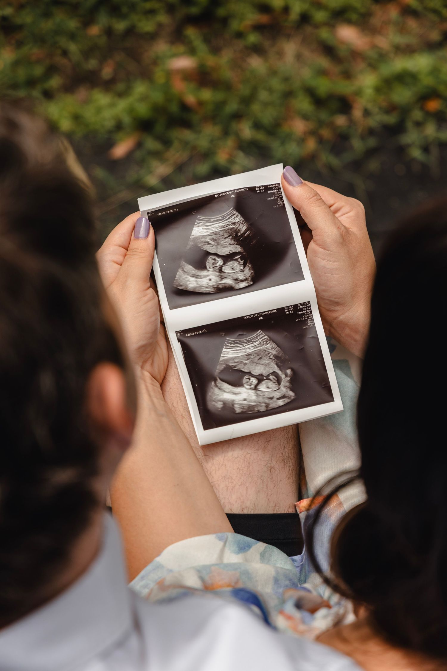 Hands holding ultrasound photos outdoors during pregnancy announcement.