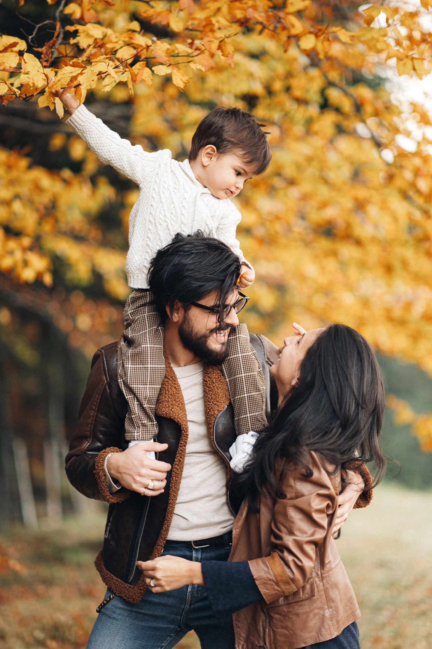 A family shares a joyful moment together under golden autumn leaves in a park.