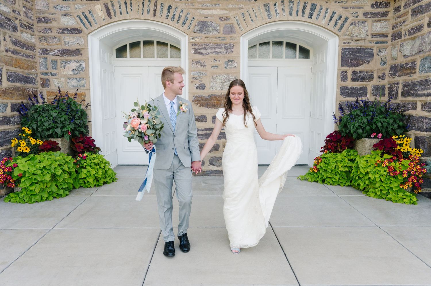 A couple in wedding attire playfully poses in front of white arched doorways.