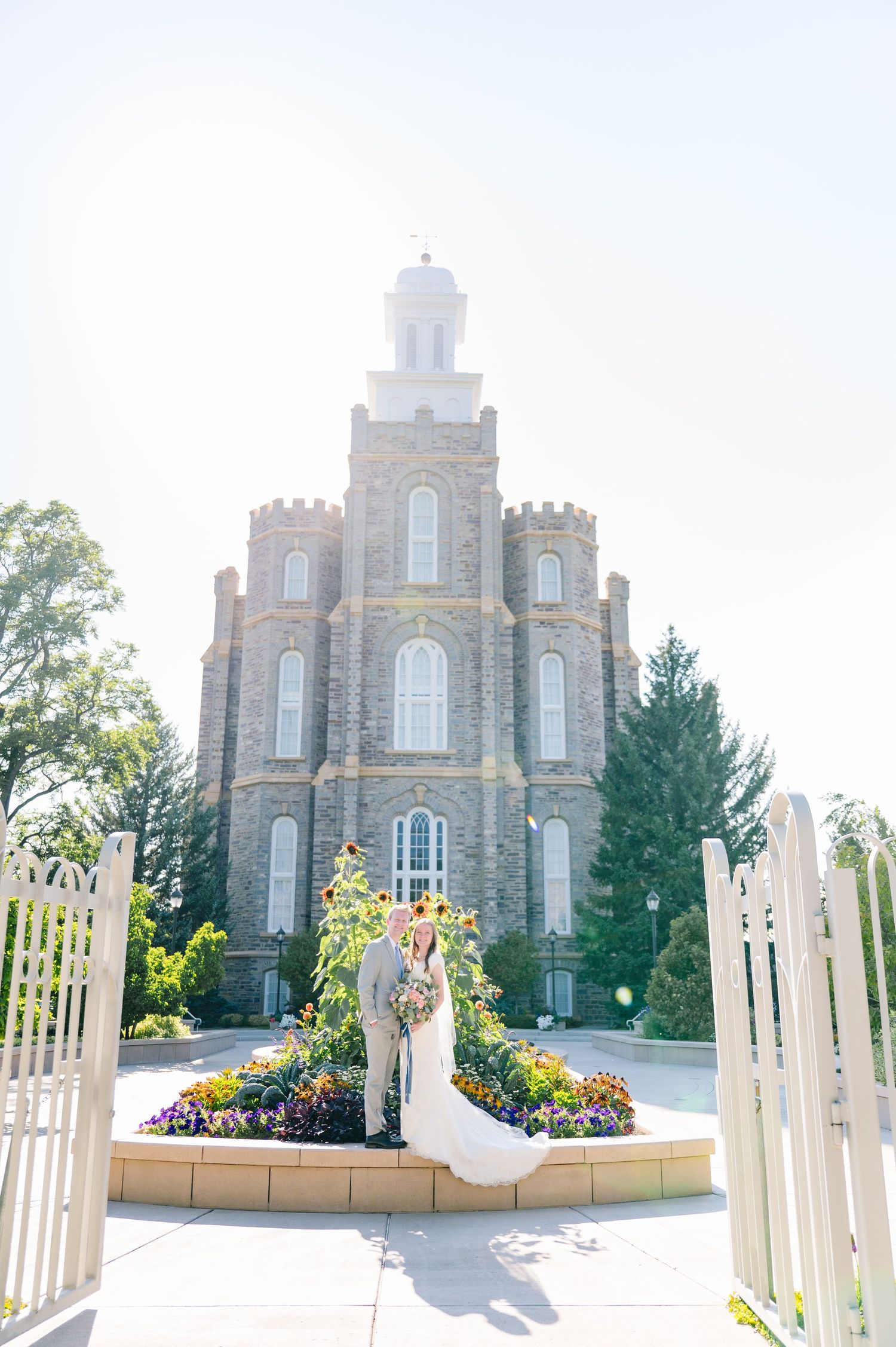 A couple in wedding attire poses in front of a historic stone temple building.