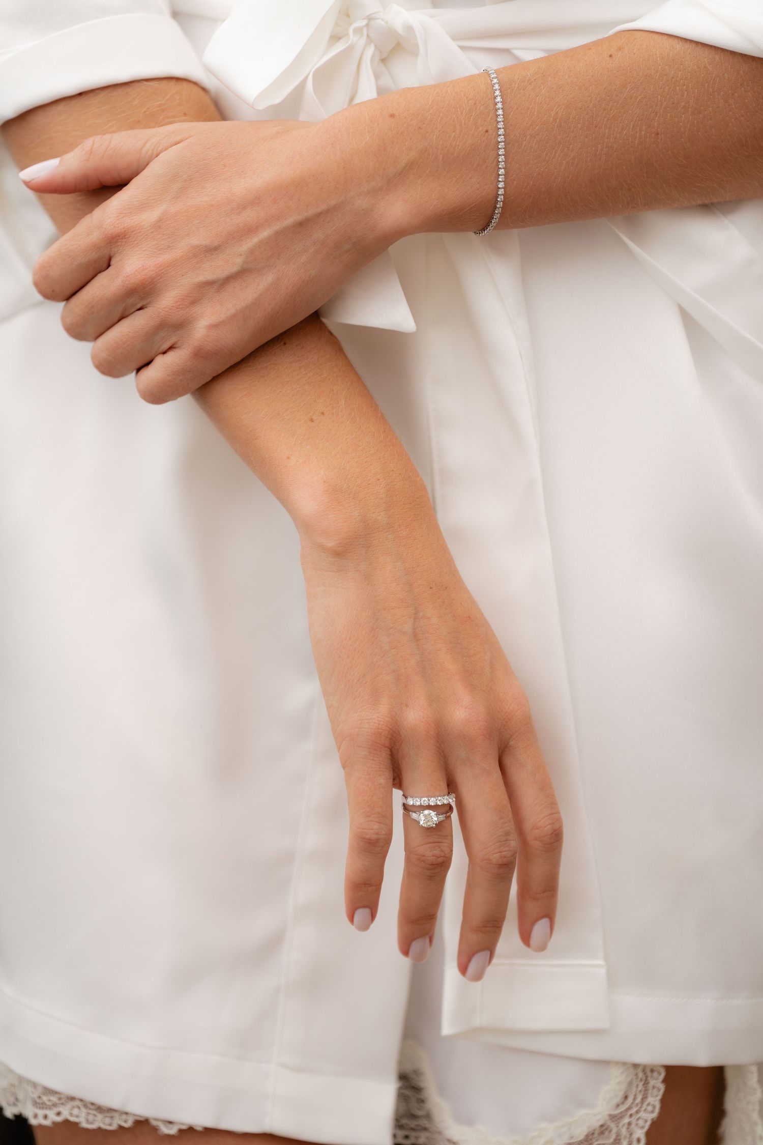 Close-up of hands wearing white lace showing engagement ring and bracelet details.