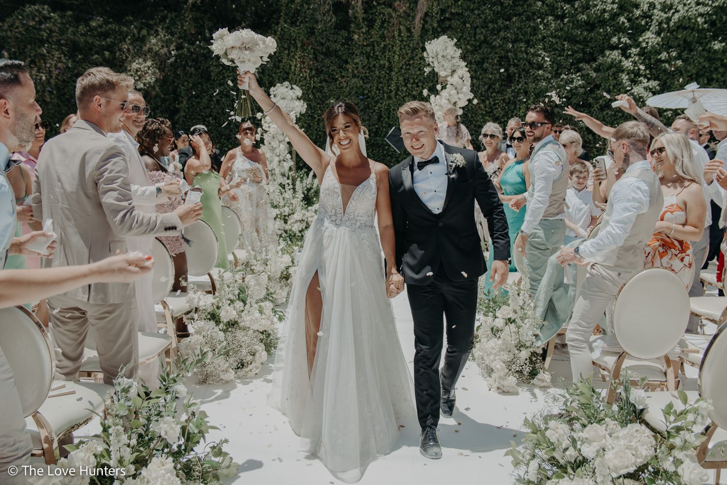 Wedding ceremony procession along a flower-lined aisle with white floral decorations.