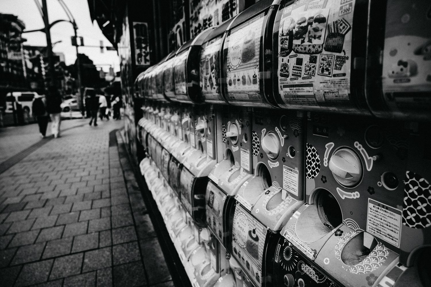 Row of colorful vending machines along a street in Japan captured in black and white.