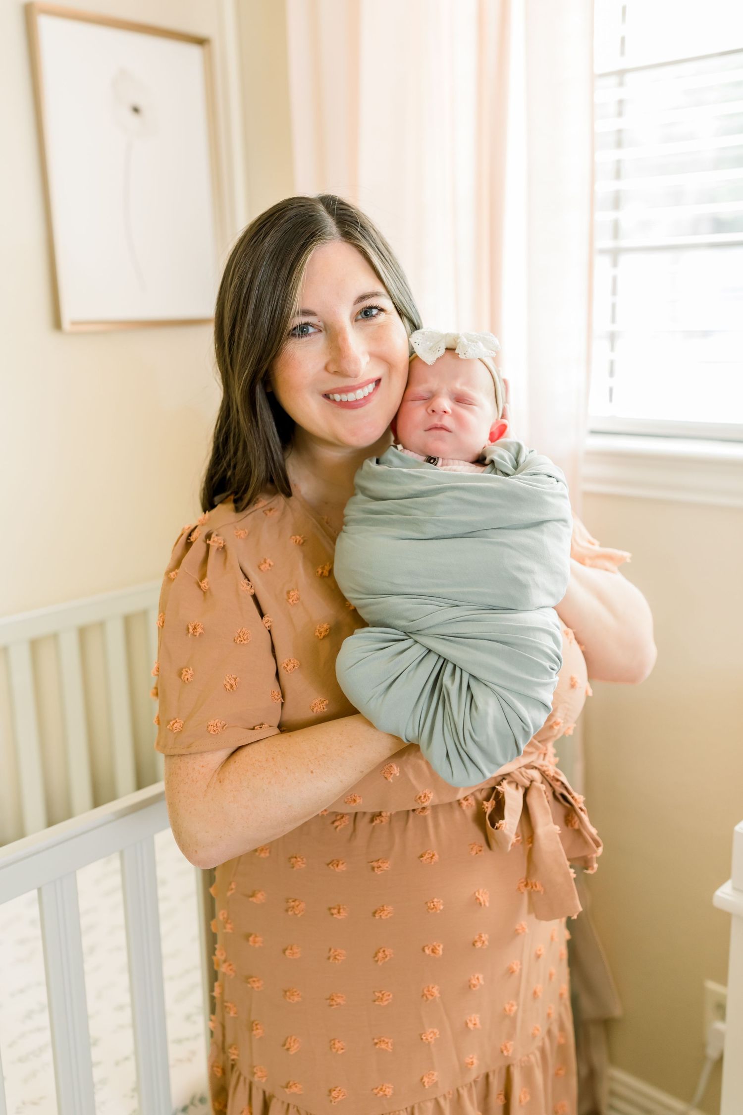 Sweet nursery moment with caregiver holding sleeping newborn wrapped in soft mint swaddle.