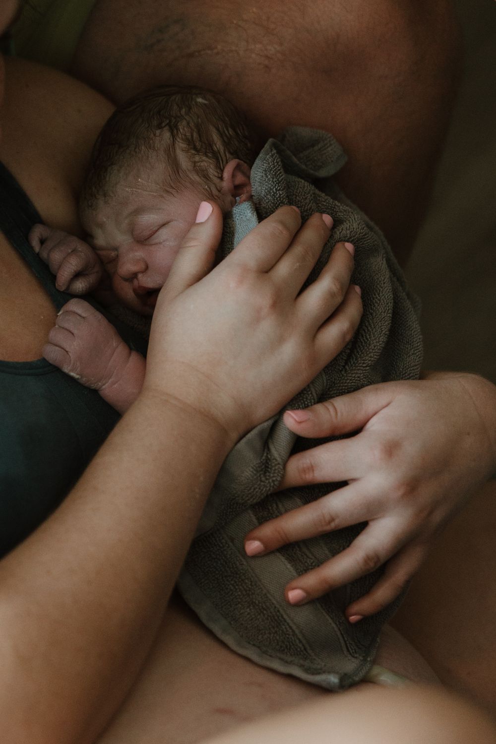 Close-up of gentle hands cradling a newborn wrapped in grey blanket.