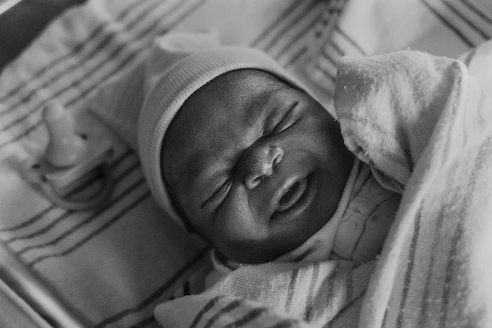 Black and white portrait of newborn with peaceful expression wearing white cap.