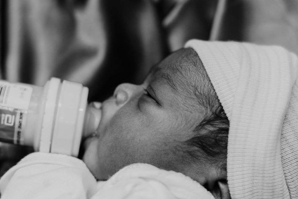 Black and white image of infant feeding from bottle while wrapped in white cloth.