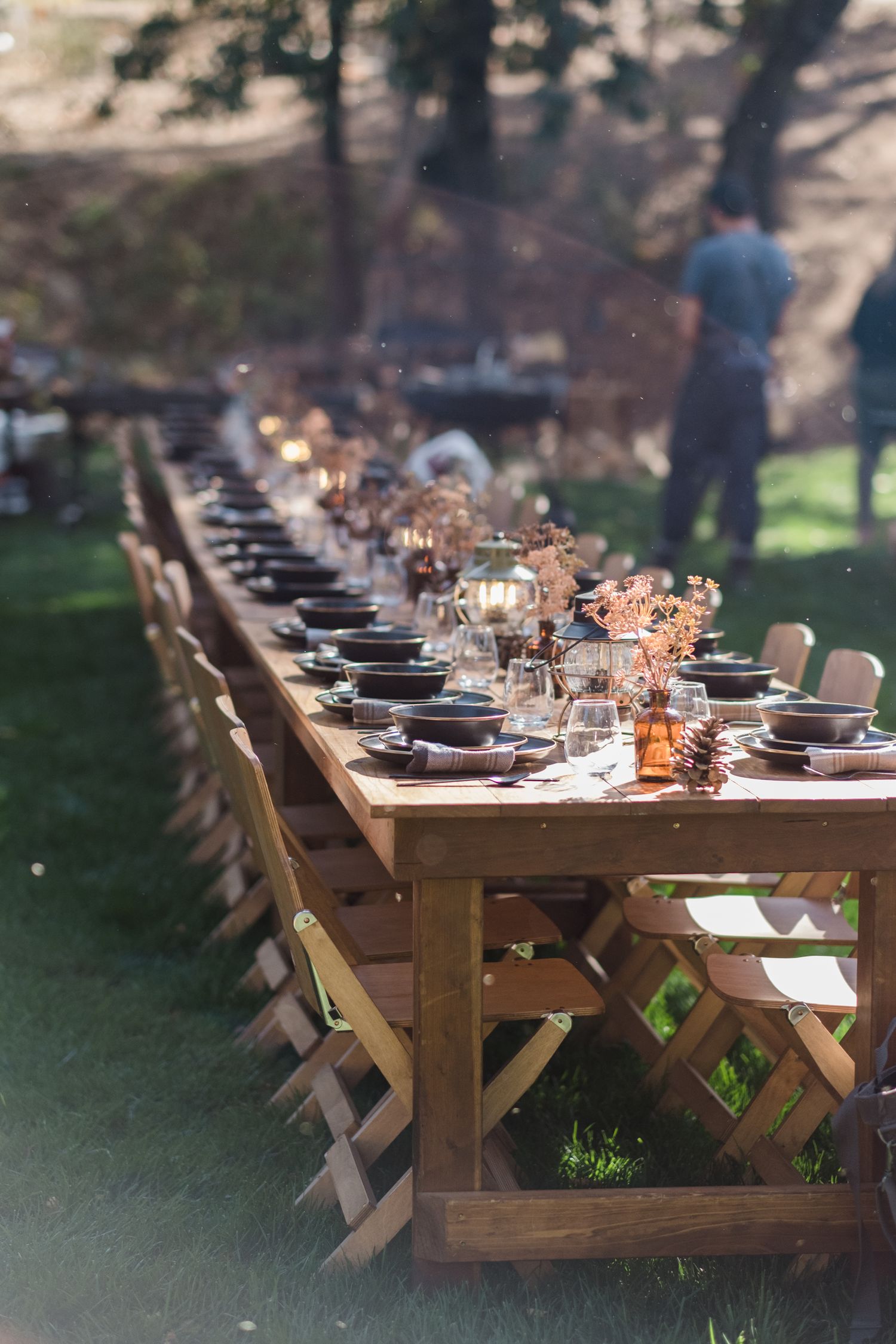 Long wooden farm table set for outdoor dining with candles and place settings.