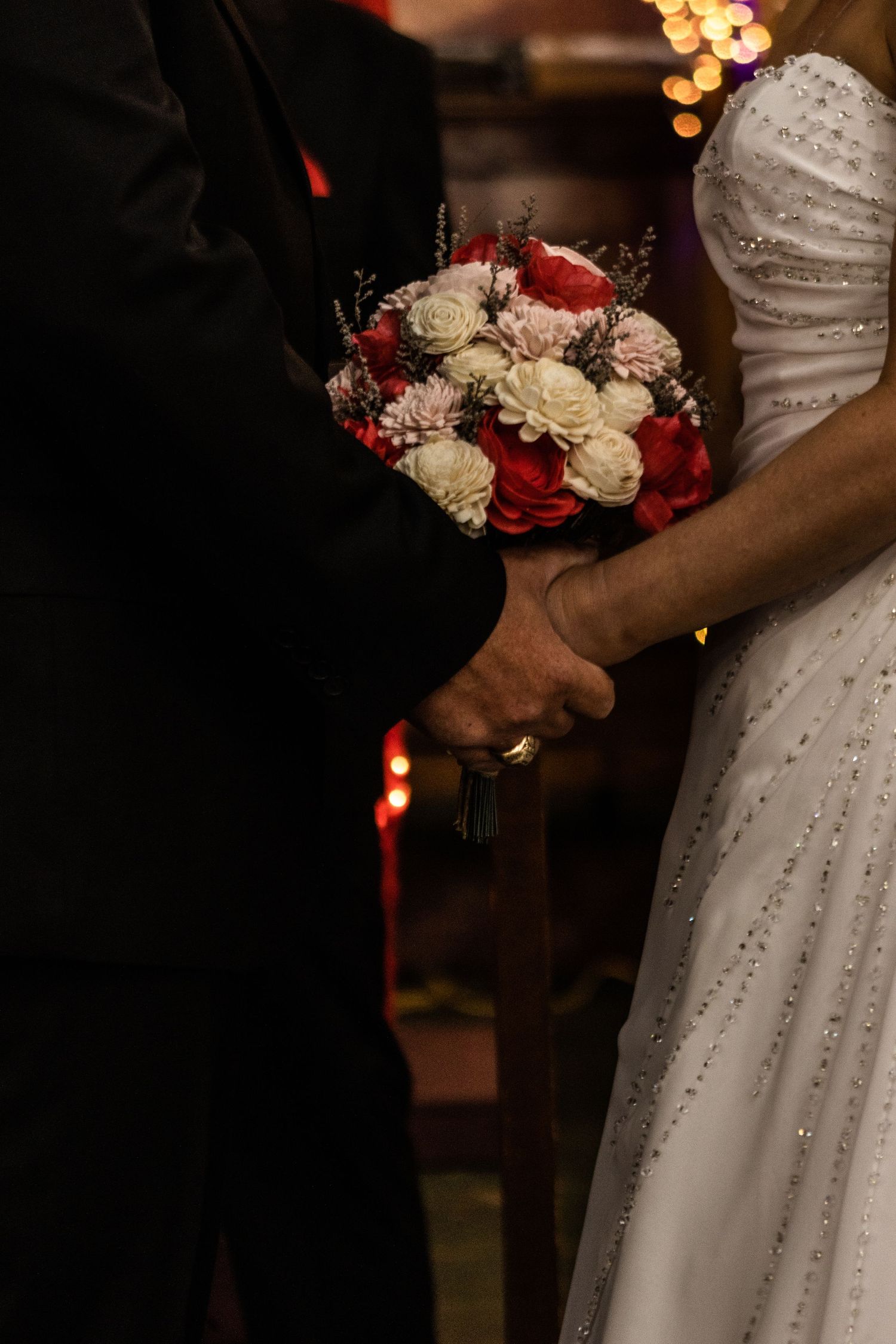 A couple at their wedding altar holds hands and her bouquet.