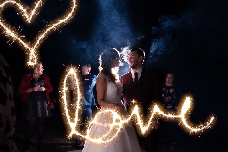 Wedding couple kisses under sparkler light art forming heart and love message.