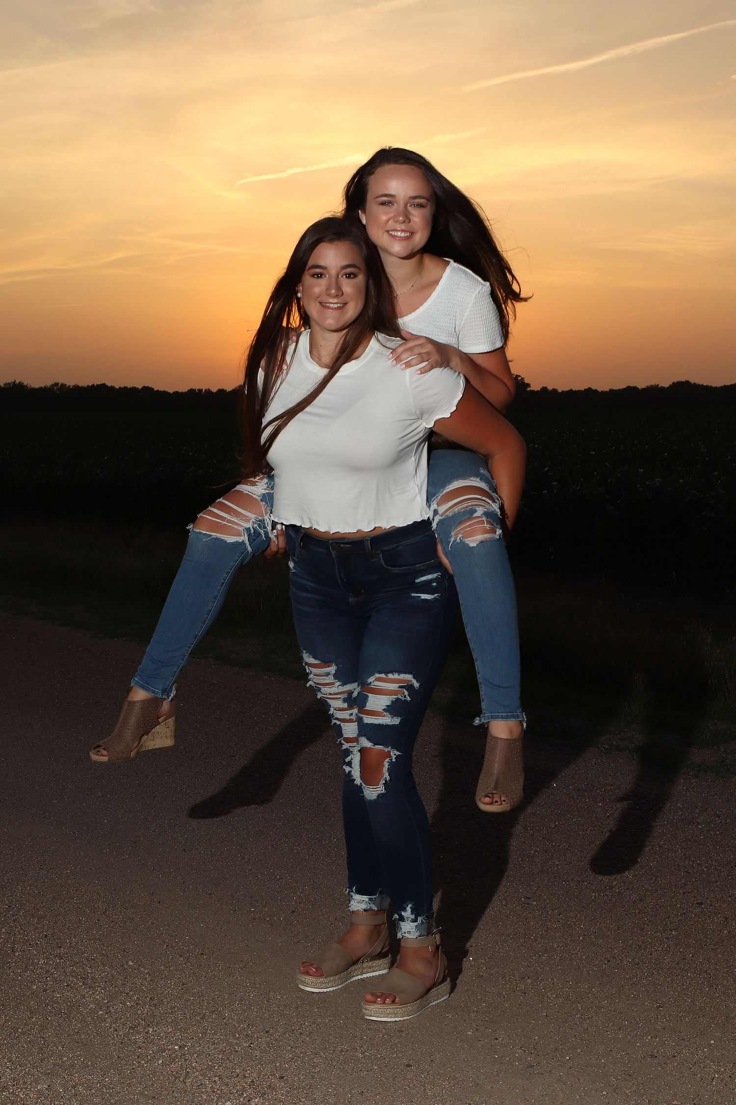 becky katzberg photography two senior girls on a gravel road at sunset wearing white shirt and jeans