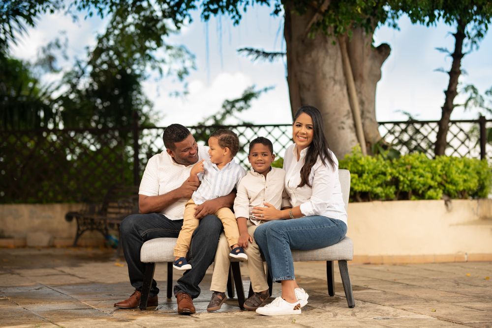 Happy family of four sitting on bench outdoors under green trees in a park setting.