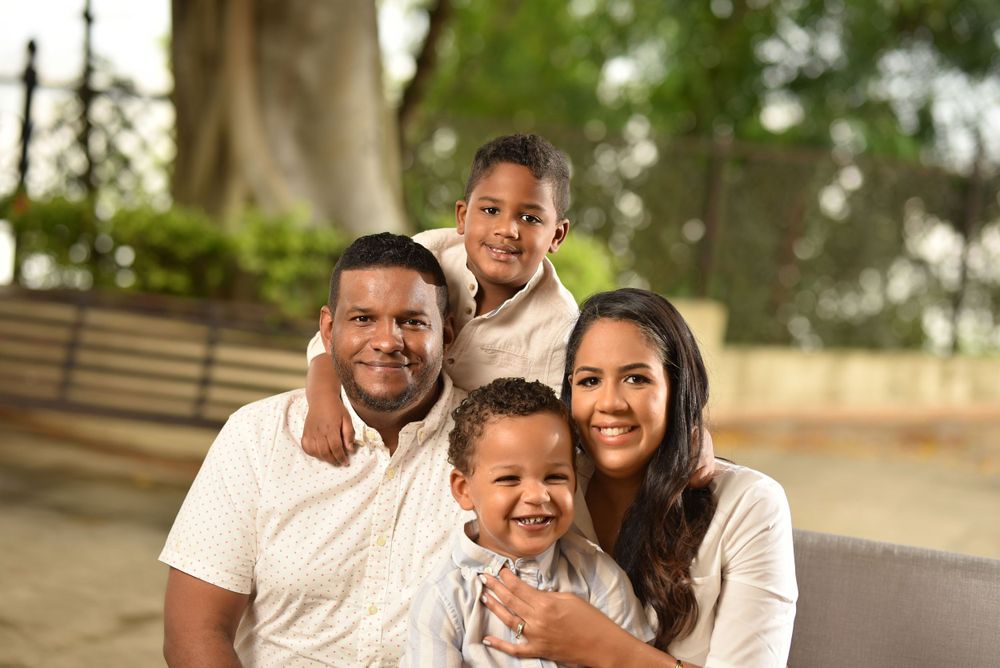 Smiling family portrait of parents and two young boys posing together in an outdoor park.