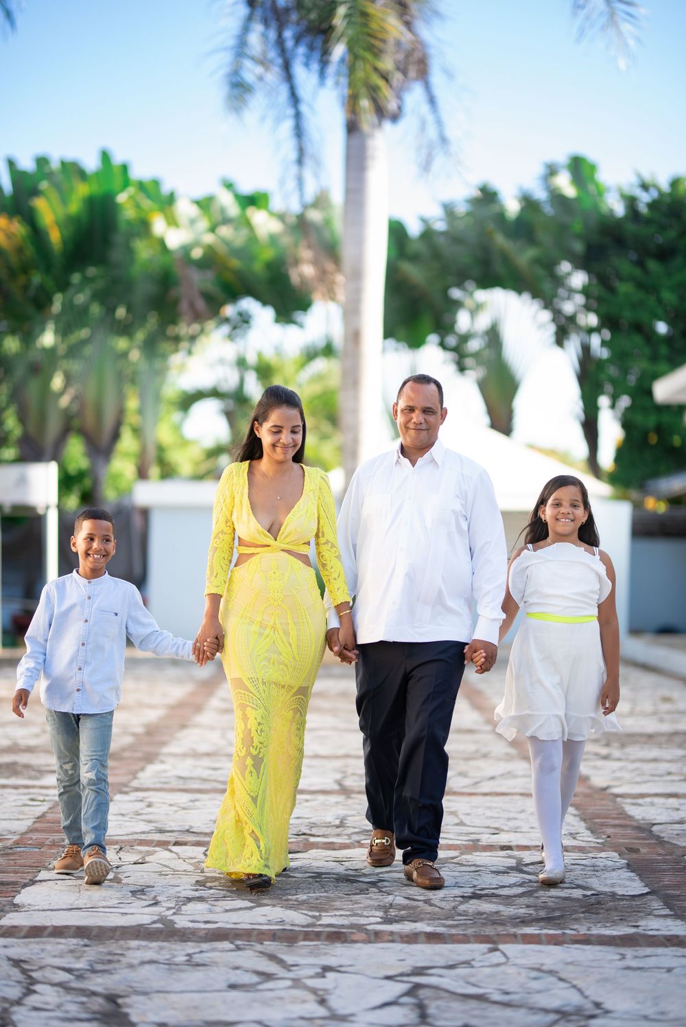 Happy family of four holding hands walking along a tropical resort pathway in coordinated outfits.