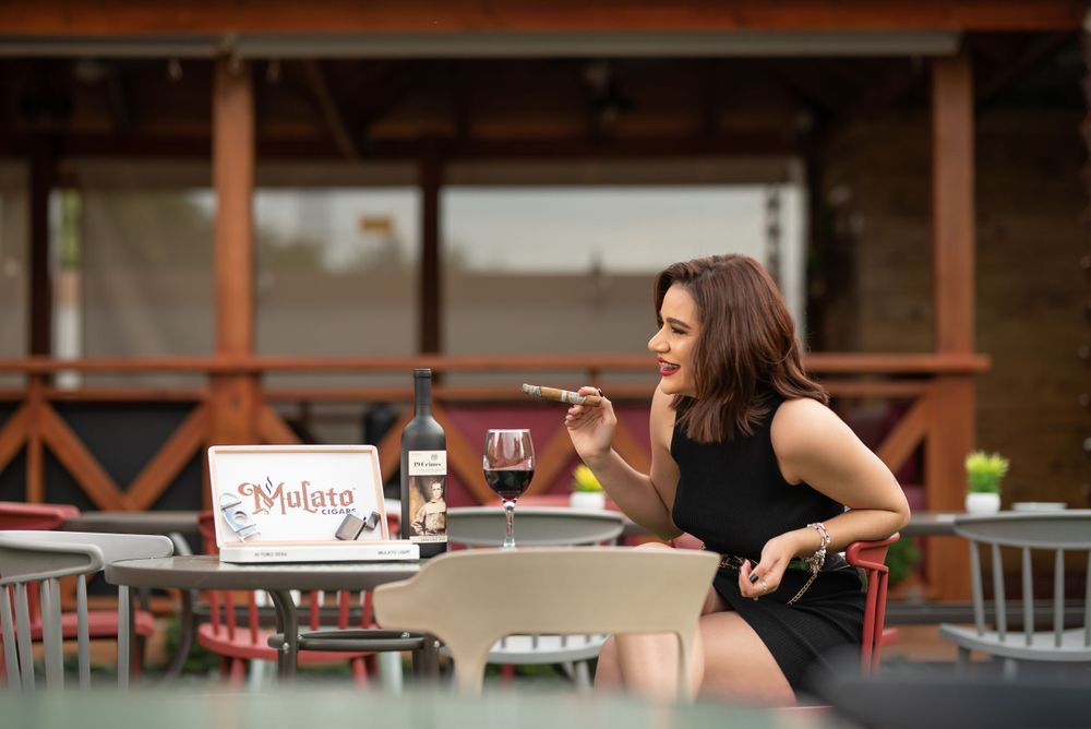 Elegant woman in black dress enjoying wine and food at an outdoor restaurant patio.
