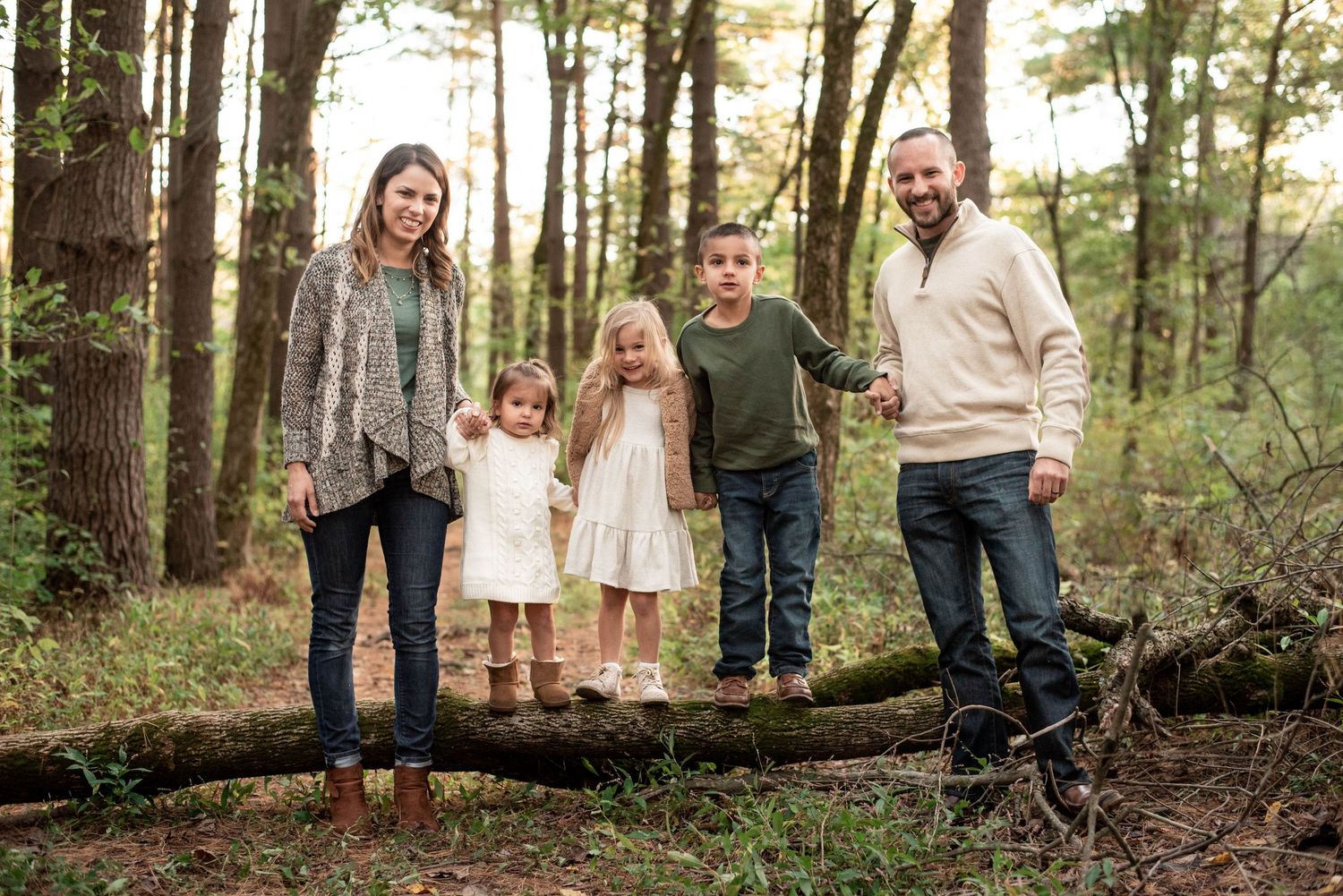 Sweet family in earth tones standing on a log in the forest.