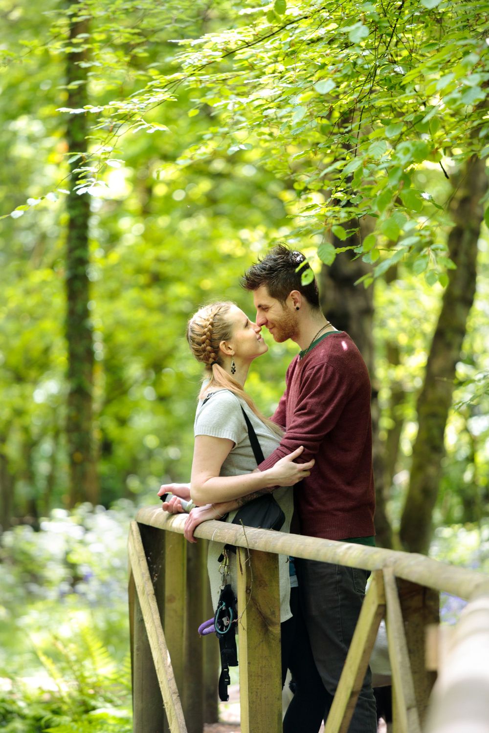 Romantic couple embracing on wooden bridge surrounded by lush green forest.