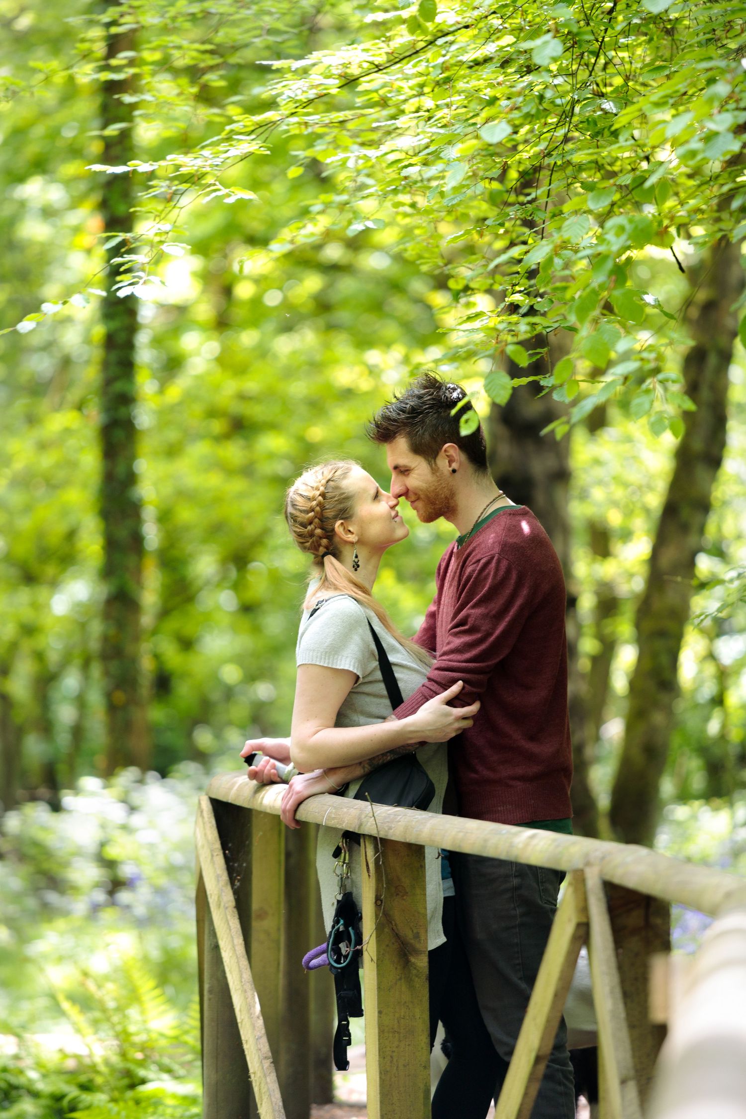 Romantic couple embracing on wooden bridge surrounded by lush green forest.