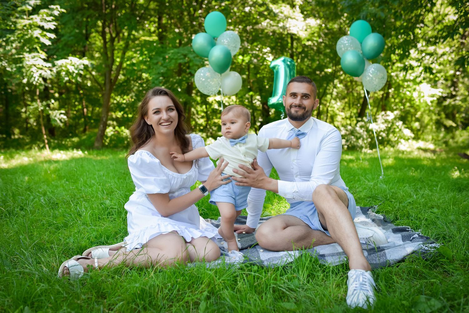 Family picnic in a park with turquoise balloons and white outfits on a sunny summer day.