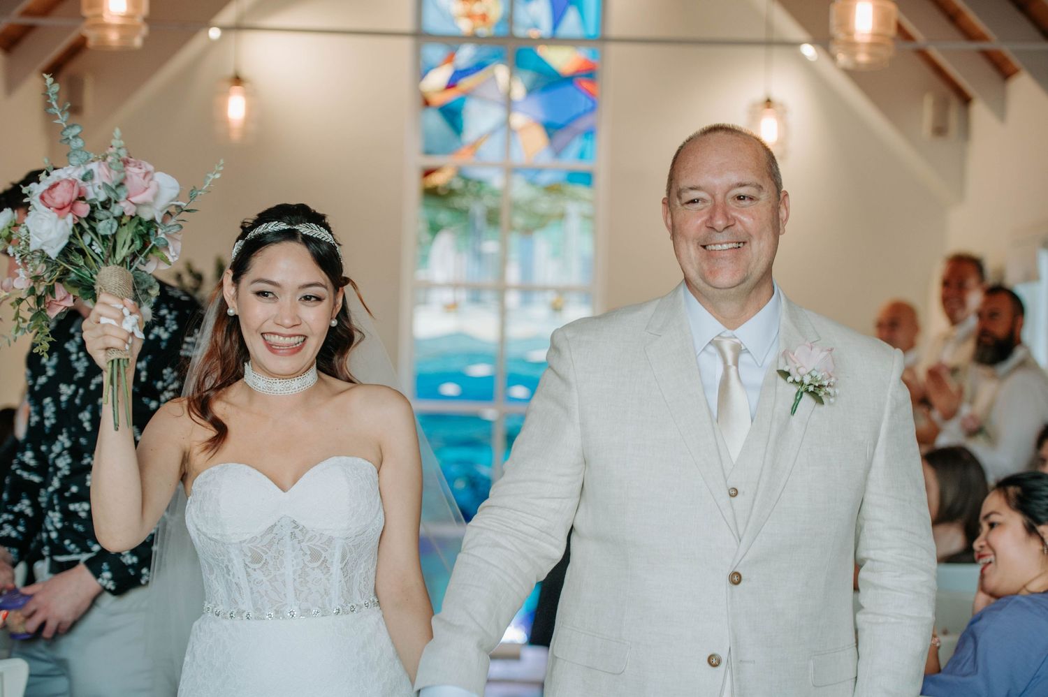 Newlyweds celebrate joyfully while walking down the aisle in a bright chapel setting.
