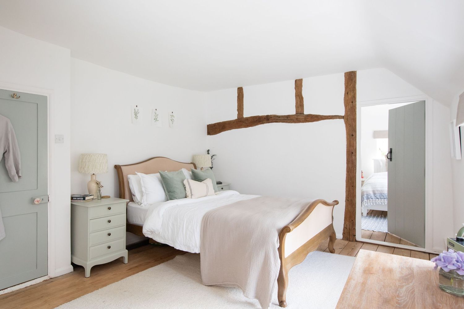Rustic bedroom with exposed wooden beams, white bedding, and sage green accents.