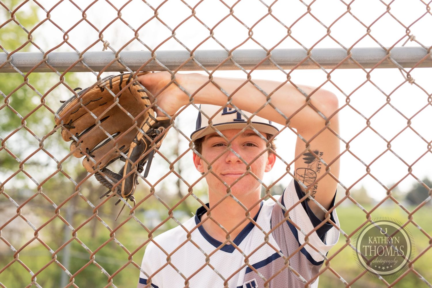 Close-up of baseball glove and uniform through chain-link fence.