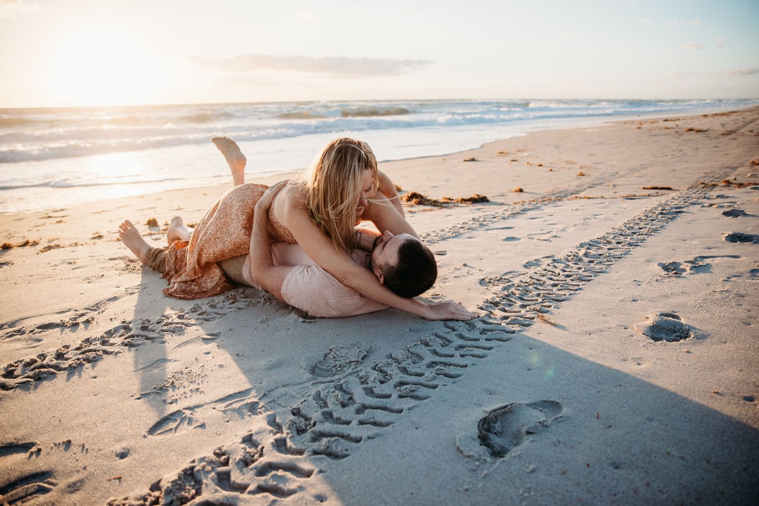 Dog and owner sharing a tender moment on a sunny beach at sunset.
