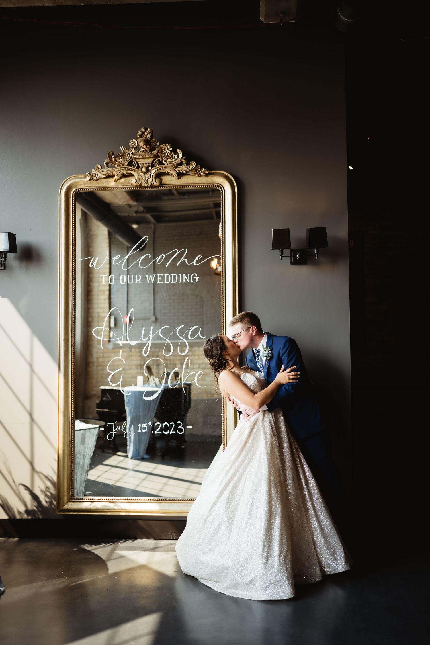 Elegant wedding welcome sign written on ornate gold mirror in dramatic lighting.