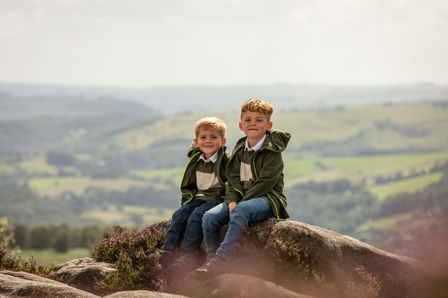 Two companions sitting on a rocky outcrop overlooking a scenic valley view.