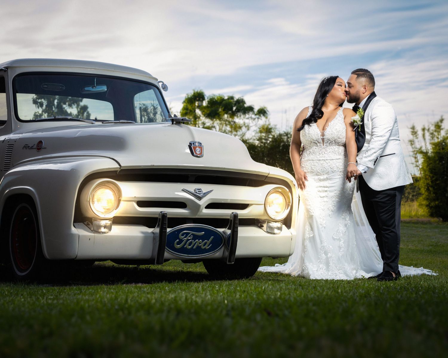 Newlyweds pose romantically by vintage Ford truck during sunset wedding photoshoot.