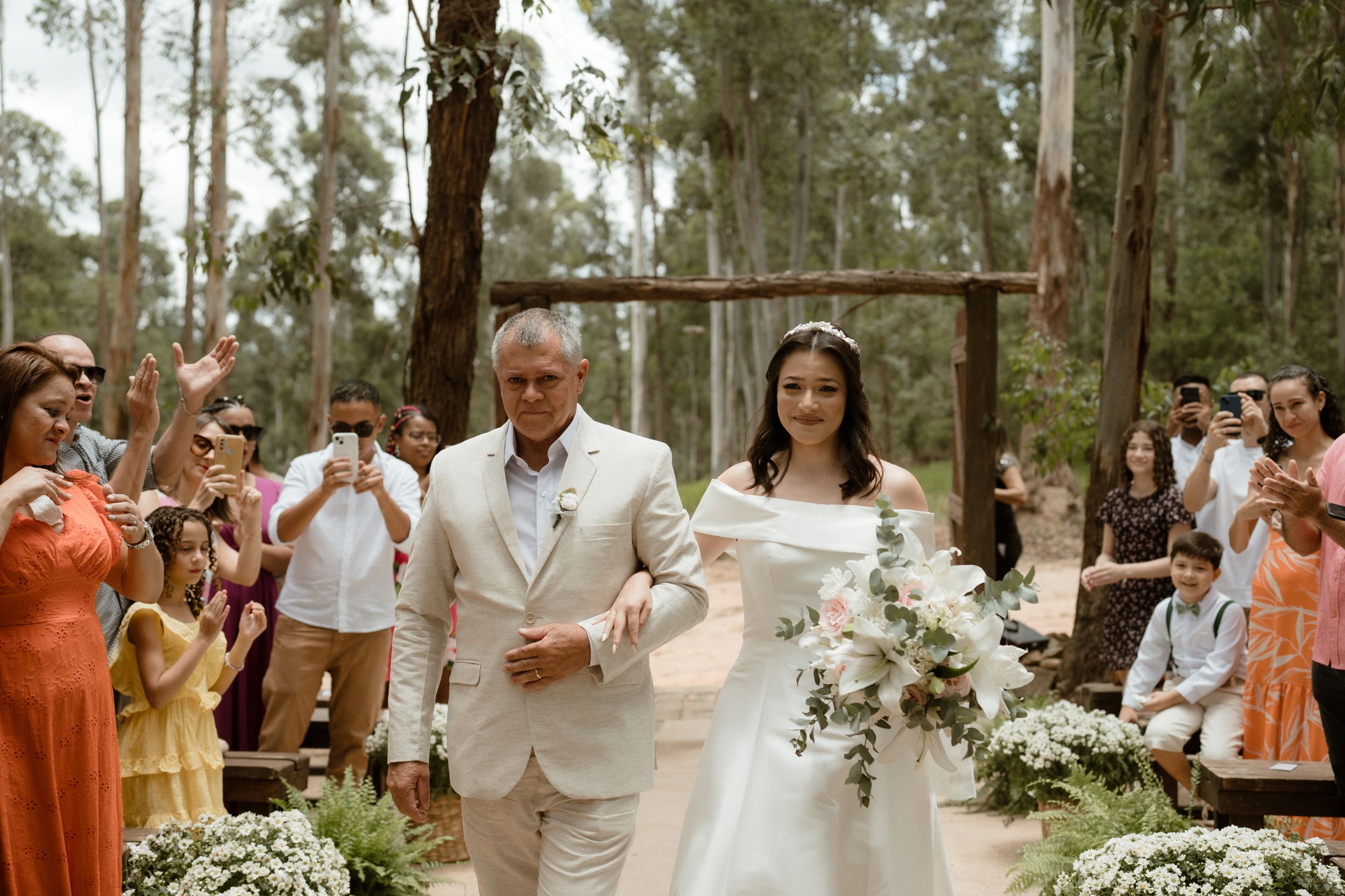 Wedding ceremony in a eucalyptus forest with guests in coral dresses watching the procession.
