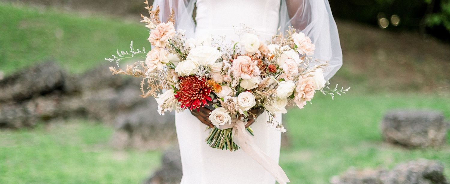 A bridal bouquet featuring blush, cream and burgundy flowers with delicate greenery.