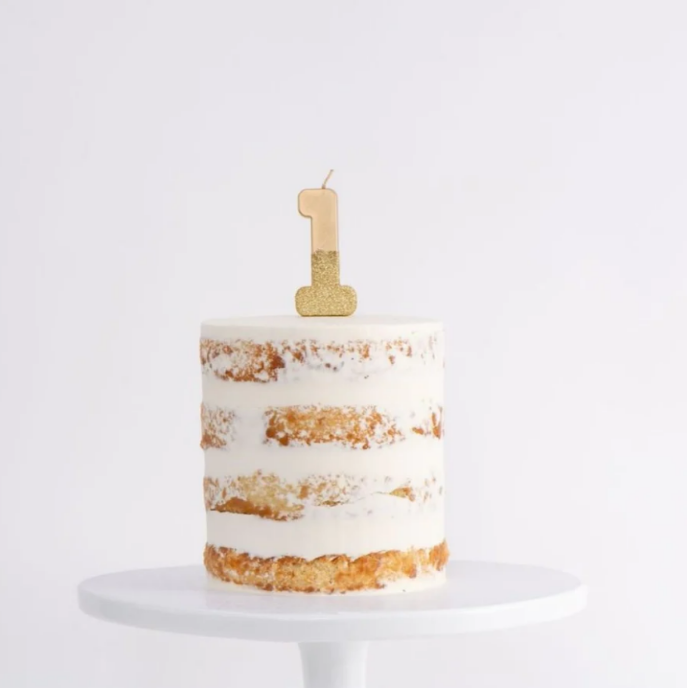Simple naked cake with white frosting and gold number one topper on white cake stand.