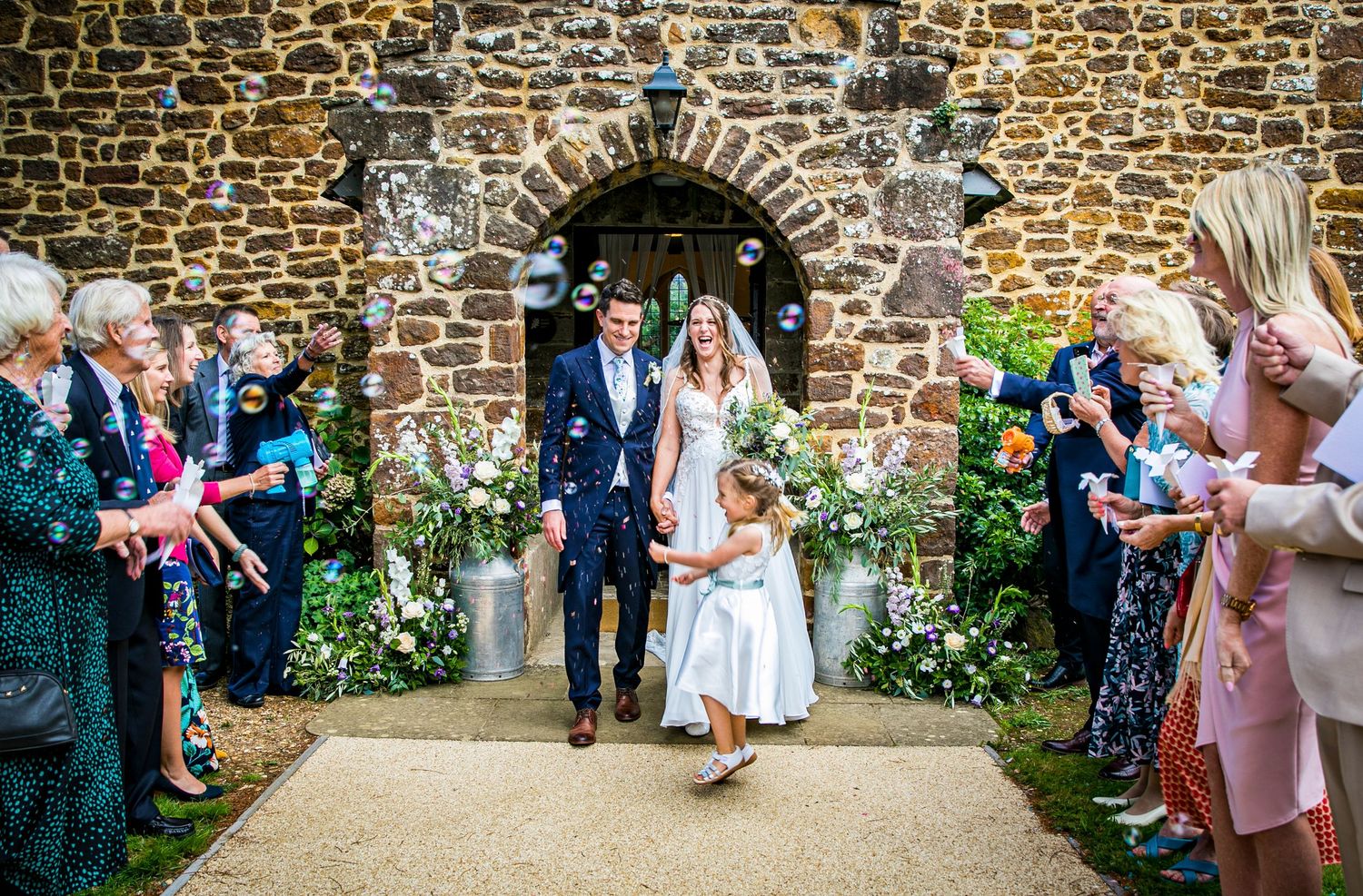 Wedding party poses against rustic stone wall for outdoor photos.