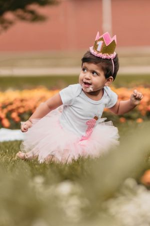 Baby wearing crown and tutu dress playing in grass during outdoor photoshoot.
