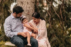 A sweet family moment captured outdoors with a small child under evergreen trees.