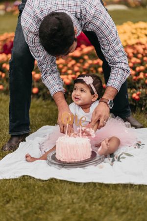 Pink first birthday cake celebration on a blanket outdoors with a tulle dress and autumn background.