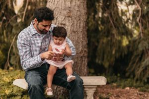 A family moment outdoors sitting together on a wooden bench near a large tree.