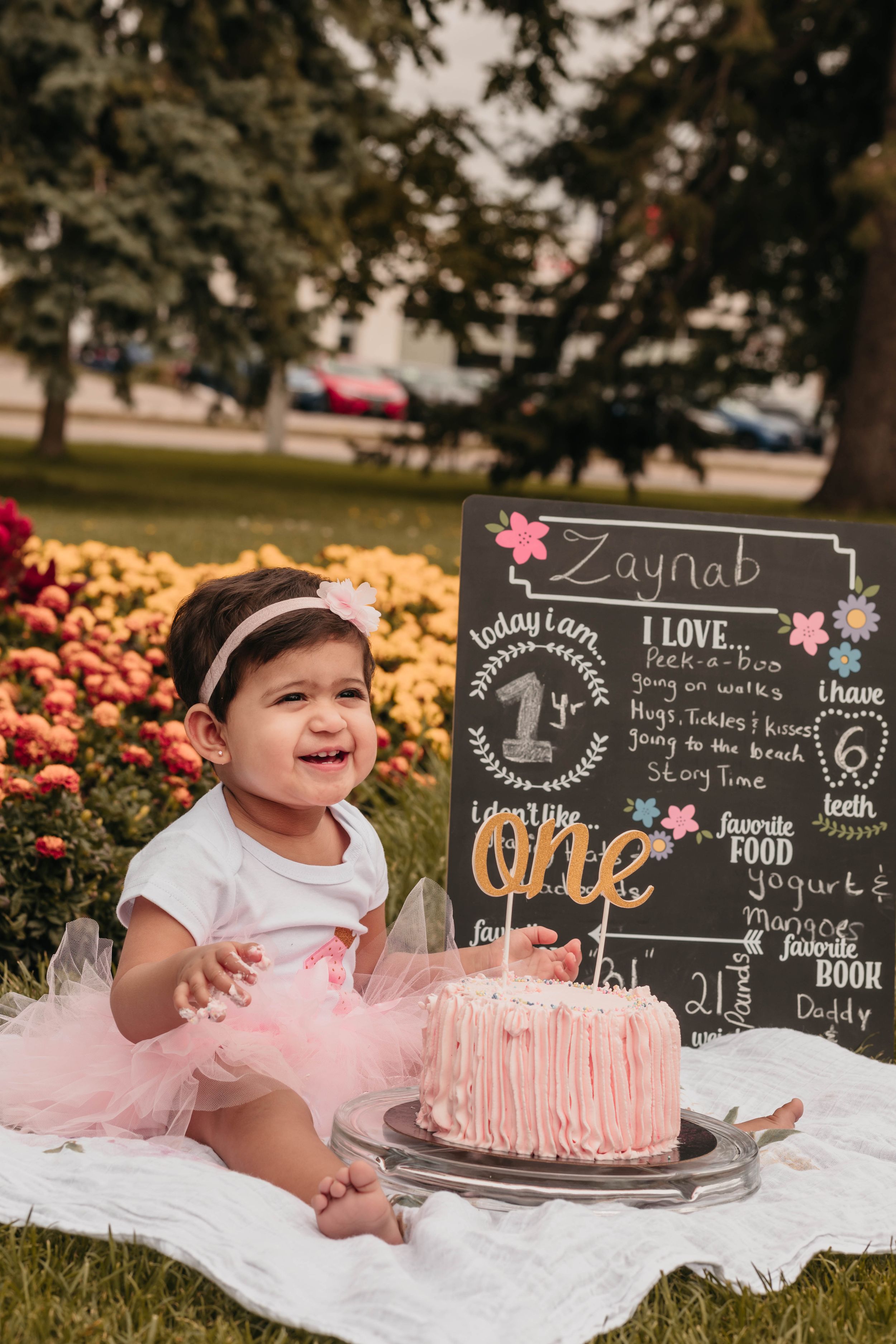 A first birthday celebration with pink cake and chalkboard milestone sign.