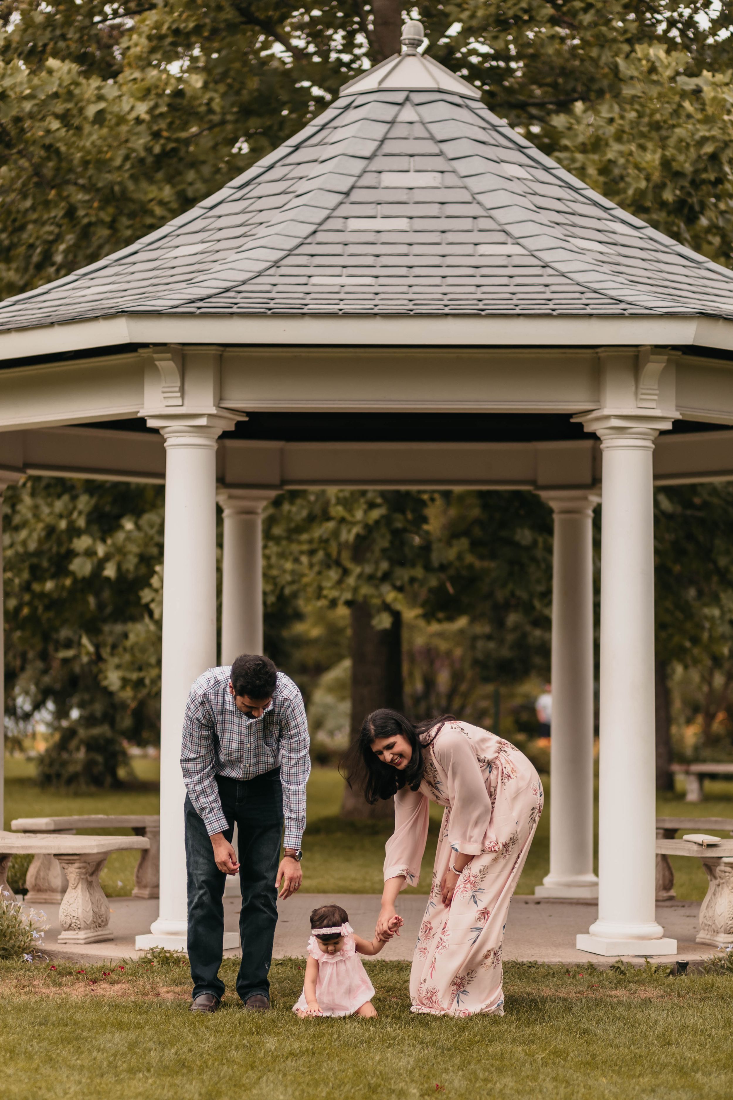 Family gathering under white gazebo in park during special occasion.