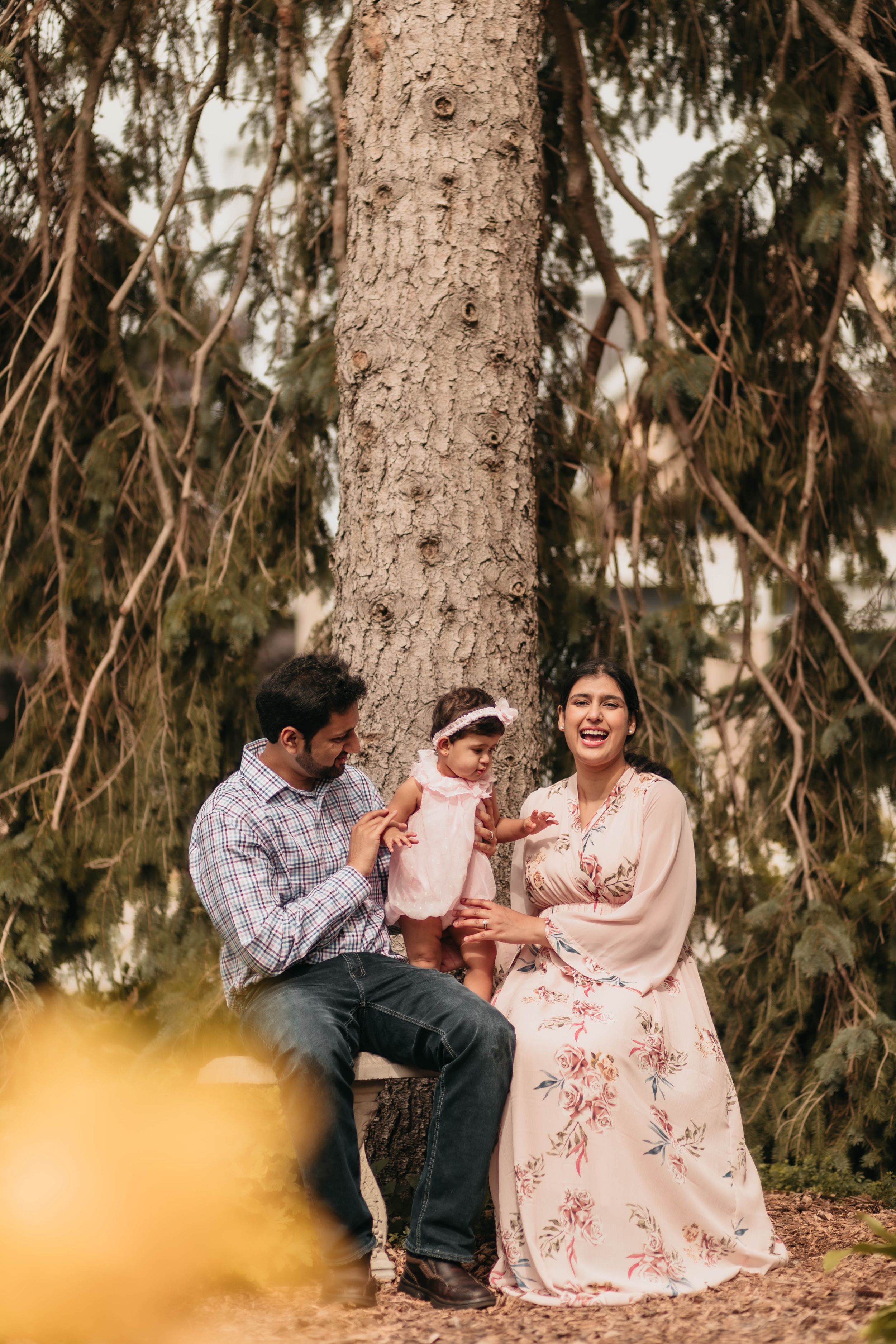 Family enjoying a candid moment together while sitting by a large pine tree.