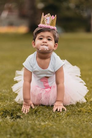 Baby in tulle dress and pink crown crawling on grass during photoshoot.