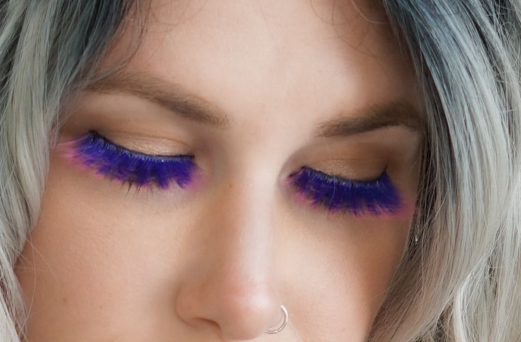 Close-up of woman with purple and blue feather false eyelashes and nose ring.