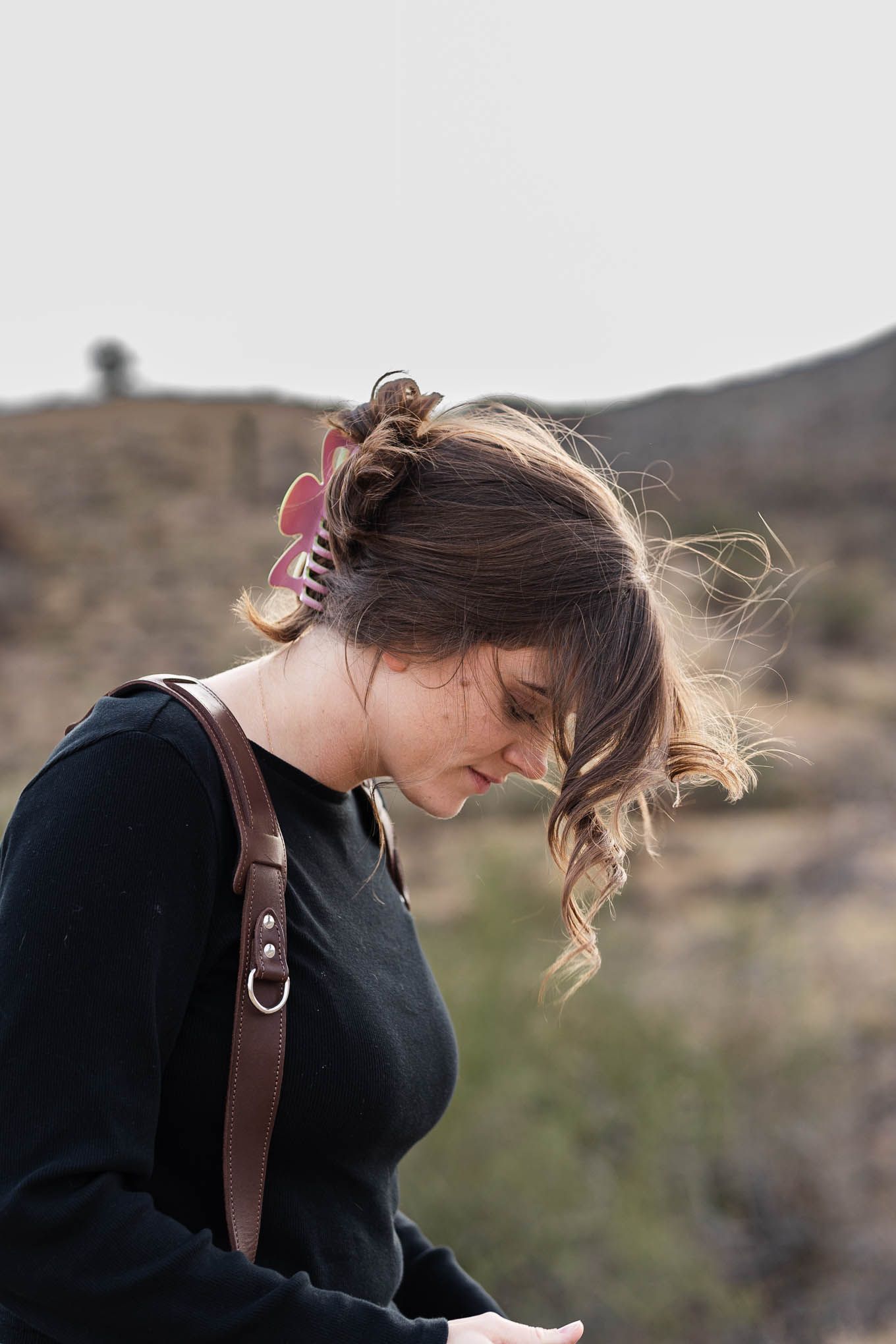 Shania hirdler Photography education - photographer looking down at her camera. claw clip in hair, smiling side profile.