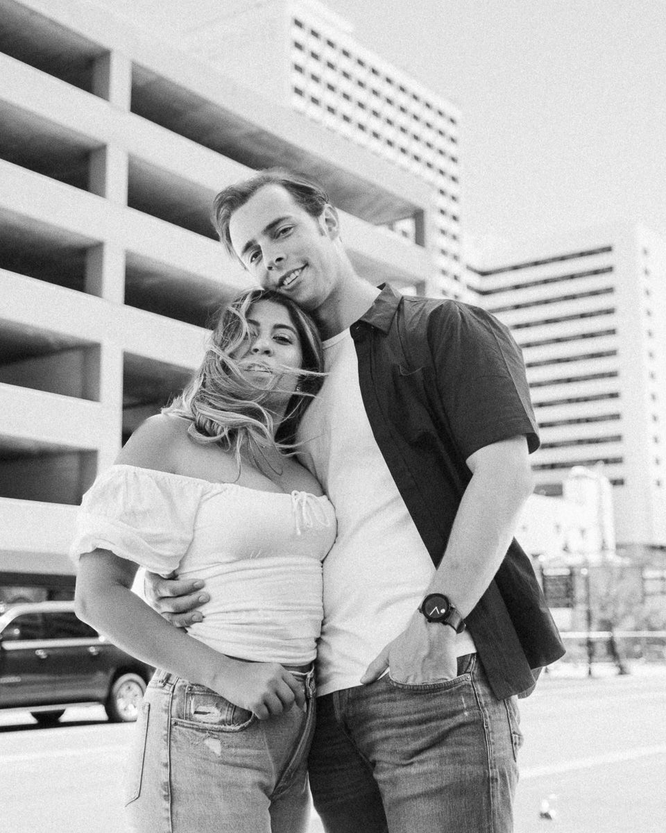A black and white photograph of a couple embracing outdoors in front of a modern building with a parking structure Reno engagement session