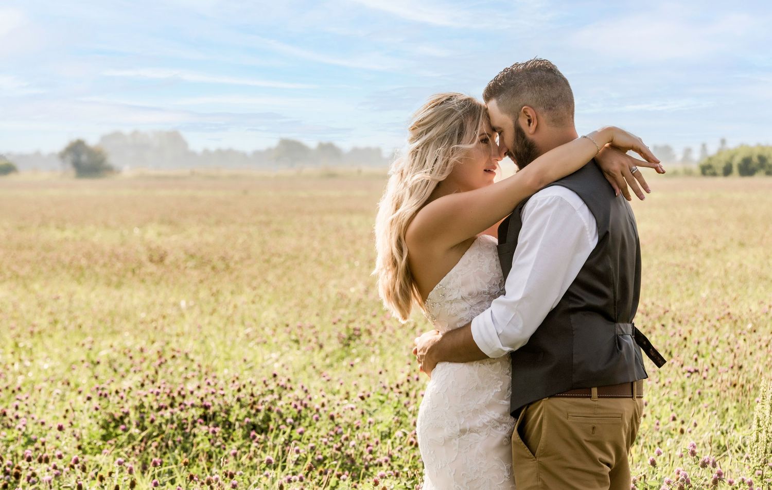 A romantic embrace in a golden field under blue skies on a sunny afternoon.